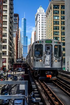 a silver train traveling through a city next to tall buildings and traffic lights with skyscrapers in the background