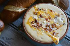 a bowl filled with cheese and bacon soup next to bread