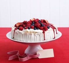 a white cake with berries and whipped cream drizzled over it on a red table