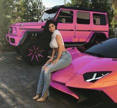 a woman sitting on the hood of a pink sports car next to a pink jeep