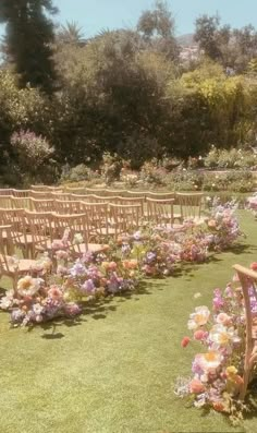 rows of wooden chairs lined up in the grass with flowers on each chair and one row of them