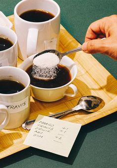 three cups of coffee on a tray with sugar and spoons next to each other