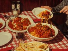 a table topped with plates and bowls filled with spaghetti next to bread sticks, cheese wedges and wine glasses