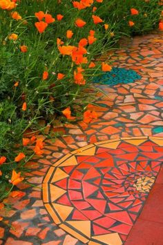 some orange flowers and green plants on the ground in front of a mosaic tile floor