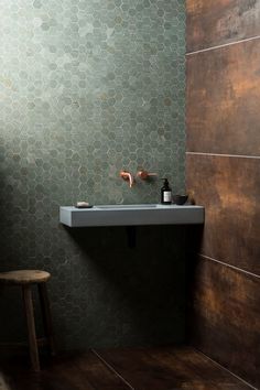 a bathroom sink sitting under a mirror next to a wooden stool in front of a tiled wall