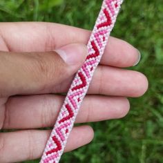 a hand holding a pink and red braided bracelet on green grass in the background