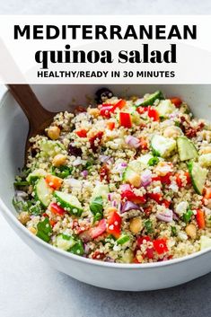 mediterranean quinoa salad in a white bowl with a wooden spoon on the side