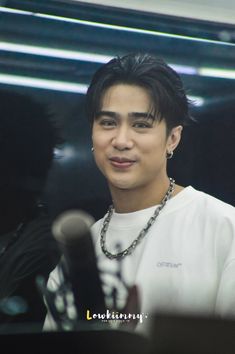 the young man is wearing a necklace and looking at the camera while standing in front of microphones