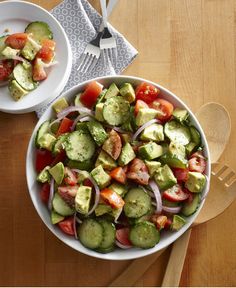 a salad with tomatoes, cucumbers and onions in a white bowl on a wooden table