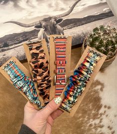 a person holding three different bracelets in front of a cow's skin background