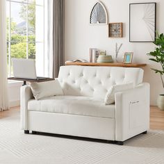 a white couch sitting in front of a window next to a table with a laptop on it