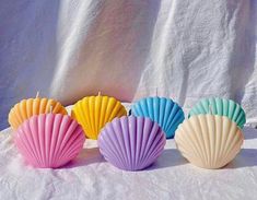 four seashell candles are lined up on a white tablecloth, with one candle lit in the middle