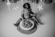 a black and white photo of a baby sitting in front of a cake with cookies on it