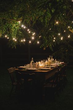 an outdoor dinner table is set with candles and wine bottles, surrounded by string lights