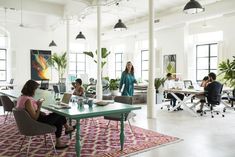 a group of people sitting at desks in an office with plants on the walls