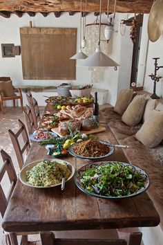 a wooden table topped with lots of food on top of a dining room table next to a couch