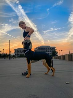 a woman standing next to a black and brown dog on top of a parking lot