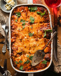 Lasagna alla bolognese in a lasagna pan with a serving spoon and fresh chopped parsley and basil.