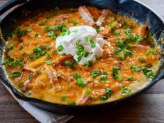 a skillet filled with food on top of a wooden table and topped with sour cream