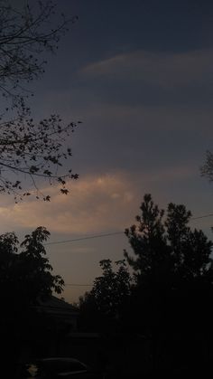 the sun is setting behind some trees and power lines in front of a dark sky