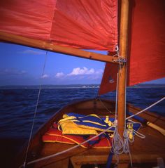 a sailboat with red sails on the water and blue sky in the back ground