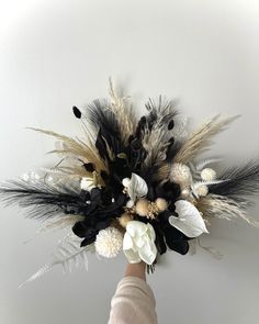 a hand holding a bouquet of flowers on top of a white wall with black and beige feathers