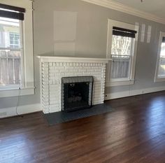 an empty living room with hard wood floors and white brick fireplace in the center area