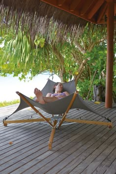 a woman laying in a hammock on a deck under a palm leaf covered roof