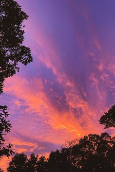 the sky is purple and orange as the sun sets in the distance with trees around it