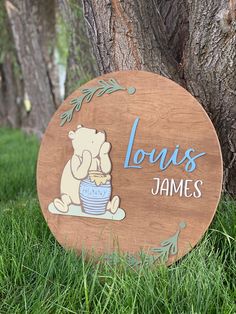 a wooden sign that says louis james with a bear holding a bowl of food in front of a tree