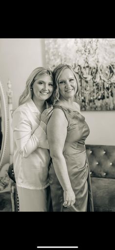 two women standing next to each other in front of a couch