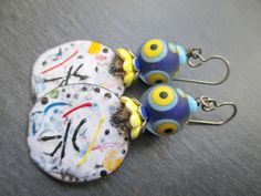 These fun earrings use abstract enameled copper charms by the madly talented Andrea of JosephineBeads in Utah. The circular charms are white with vibrant lines and dots in black, yellow, blue and red. They have the feeling of a shower of confetti after a big celebration. Above the colorful charms are yellow ceramic flower bead caps followed by nay and silver enameled flower bead caps. The hold wonderfully whimsical lamp-work glass beads by Unventdeliberte in France. The matte lamp-work glass bea Whimsical Lamp, Lines And Dots, Dichroic Glass Earrings, Abstract Earrings, Lampwork Earring, Soldering Jewelry, Yellow Ceramics, Funky Earrings, Art Earrings