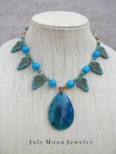 "Dragon Veins Agate Pendant with Quartzite Large Beads, Magnesite Leaves and Czech Glass Beads. This is another statement piece that cannot be missed.  Deep aqua tones are complemented by the brass findings and brass accents in the leaves.  It is 16\" in length. The pendant bail and toggle clasp are brass plated." Handmade Turquoise Agate Necklace, Beaded Turquoise Agate Necklace, 2024 Jewelry, Turquoise Necklaces, Czech Glass Necklace, Pendant Bail, Large Beads, Agate Pendant Necklace, Dragon Vein Agate