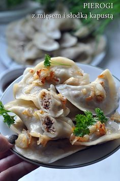 a person holding a plate of dumplings with broccoli on it and another dish in the background