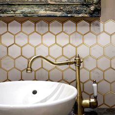 a bathroom sink with a gold faucet and marble counter top in front of a painting