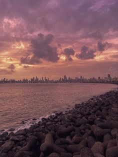 a view of the city skyline from across the water at sunset with rocks in foreground