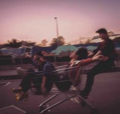 a group of young men riding on the back of a shopping cart in a parking lot