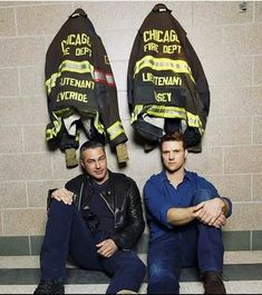 two men sitting next to each other in front of fire fighter's jackets on the wall