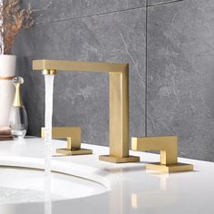 two gold faucets on a white countertop next to a vase with flowers