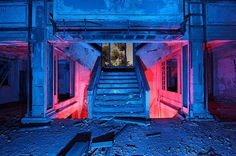 an abandoned building with red and blue light coming from the top floor to the bottom