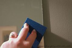 a person is cleaning the wall with a blue sponge on it's side and another hand holding something in front of them