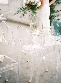 a woman in a white dress standing next to some clear chairs