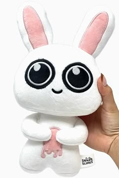 a hand holding a white stuffed animal with big eyes