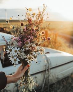 a person holding a bouquet of flowers next to an old car on the side of the road