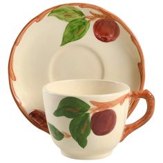 a cup and saucer with fruit designs on the rim, sitting next to each other