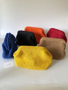 four different colored knitted bags sitting on top of a white table next to each other