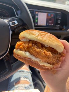 a hand holding a sandwich in front of a car steering wheel with the dash light on