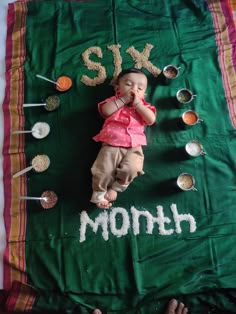 a baby laying on top of a green blanket with spoons and spices around it