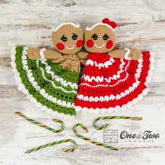 two crocheted dolls are sitting next to candy canes on a wooden surface