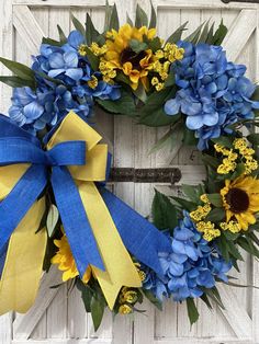 a blue and yellow wreath with sunflowers, leaves and ribbon hanging on a white door